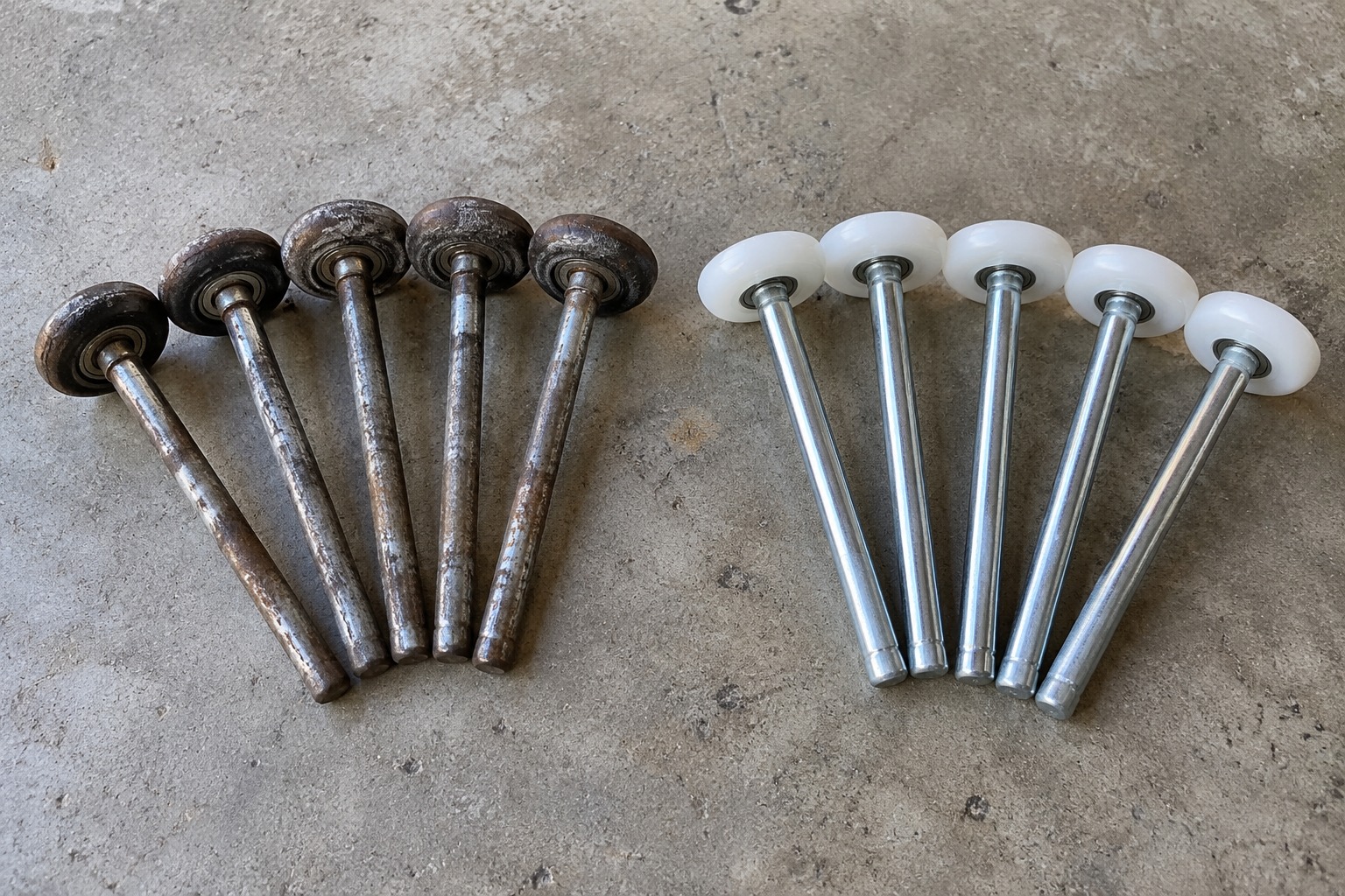 Worn steel garage door rollers beside new white nylon replacement rollers